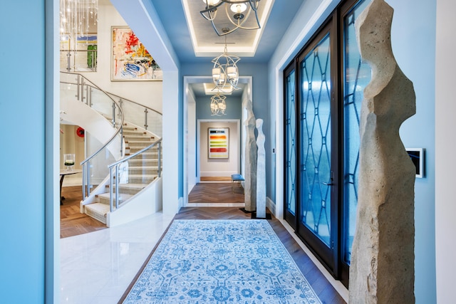 foyer entrance featuring parquet flooring, an inviting chandelier, and a raised ceiling