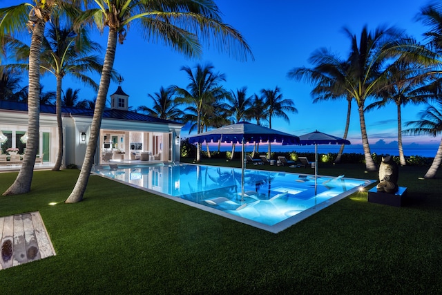 pool at dusk with a patio area and a lawn