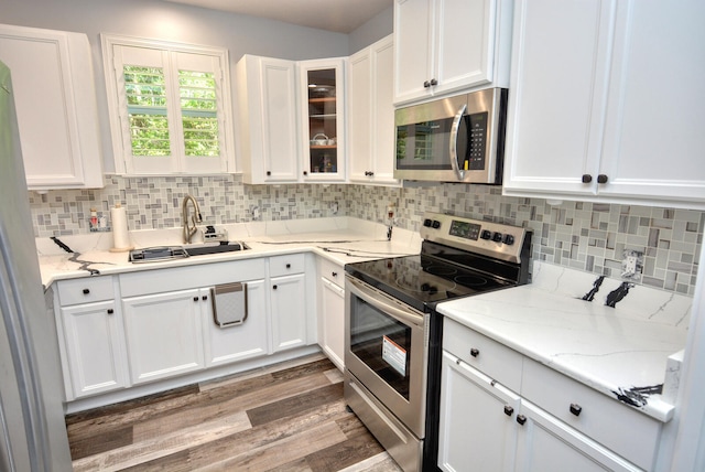 kitchen featuring light stone countertops, appliances with stainless steel finishes, sink, wood-type flooring, and white cabinets