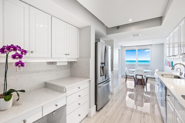 kitchen with appliances with stainless steel finishes, tasteful backsplash, white cabinets, light stone counters, and sink