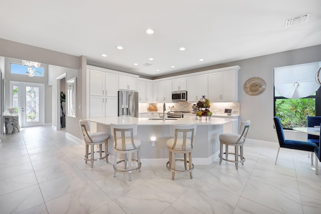 kitchen featuring a kitchen breakfast bar, white cabinetry, a large island, stainless steel appliances, and decorative backsplash