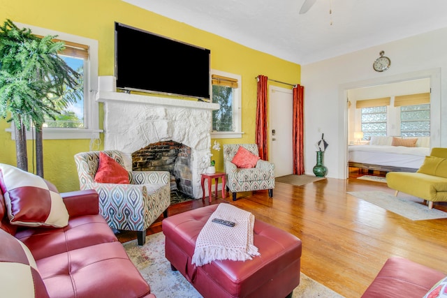 living room with a stone fireplace, light hardwood / wood-style flooring, and ceiling fan