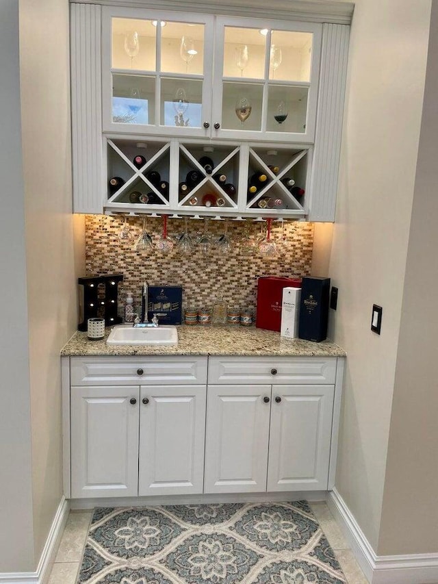 bar with light tile patterned flooring, sink, white cabinetry, light stone countertops, and decorative backsplash