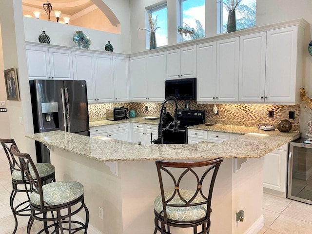 kitchen featuring light stone counters, black appliances, white cabinetry, and a kitchen breakfast bar