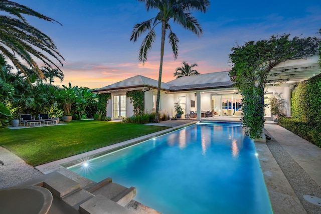 pool at dusk with a lawn and a patio