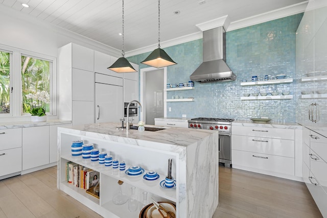 kitchen featuring high end range, wall chimney exhaust hood, white cabinetry, sink, and a kitchen island with sink