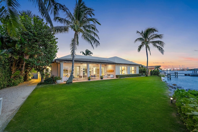 back house at dusk with a lawn and a water view