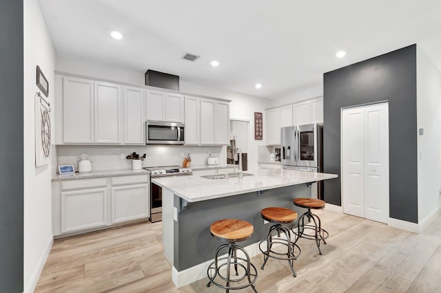 kitchen with visible vents, a kitchen bar, a sink, light wood-style flooring, and appliances with stainless steel finishes