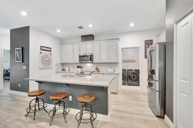 kitchen with a kitchen bar, a sink, baseboards, stainless steel appliances, and washer and clothes dryer