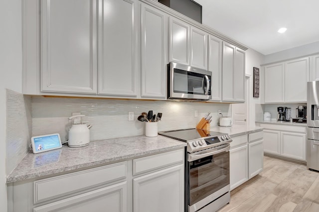 kitchen featuring decorative backsplash, light stone countertops, white cabinets, stainless steel appliances, and light wood-style flooring