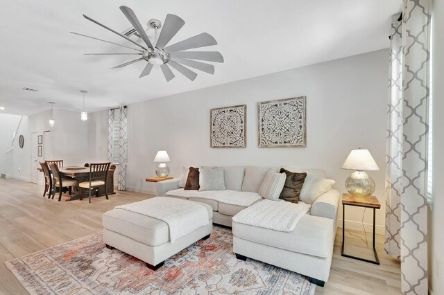 living area featuring baseboards, visible vents, ceiling fan, and light wood-style floors