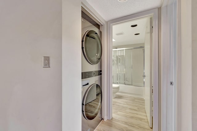 clothes washing area featuring a textured ceiling, stacked washer and dryer, and light hardwood / wood-style floors