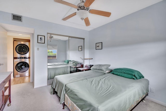 bedroom with a closet, light colored carpet, ceiling fan, and stacked washer and clothes dryer