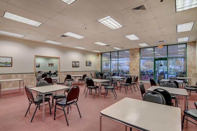 dining area featuring carpet flooring, a drop ceiling, and a wall of windows