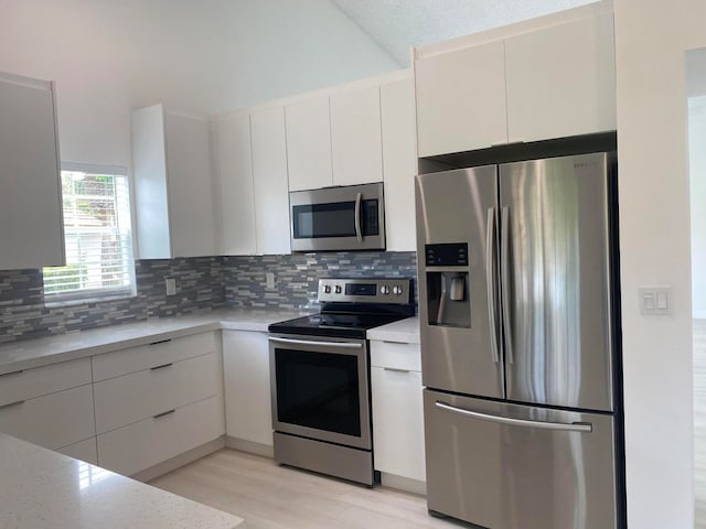 kitchen with appliances with stainless steel finishes, white cabinetry, light hardwood / wood-style floors, and tasteful backsplash