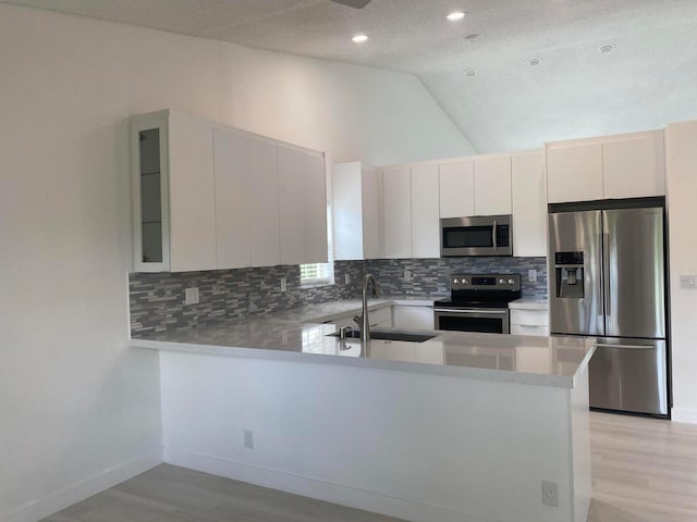 kitchen featuring sink, kitchen peninsula, white cabinetry, stainless steel appliances, and vaulted ceiling