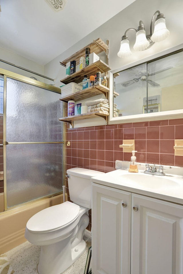 full bathroom featuring vanity, bath / shower combo with glass door, tile walls, toilet, and decorative backsplash