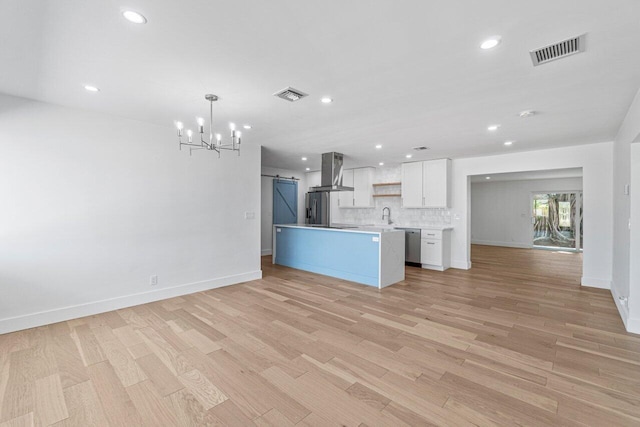 kitchen featuring white cabinets, light hardwood / wood-style floors, wall chimney exhaust hood, and a barn door