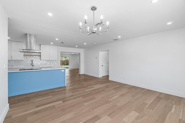 kitchen with light wood-type flooring, wall chimney range hood, hanging light fixtures, and white cabinets