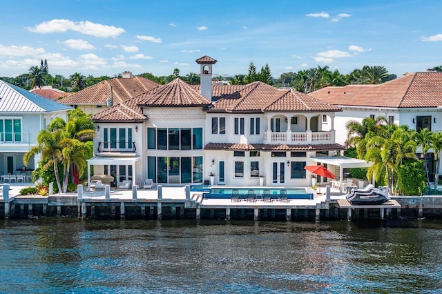 rear view of house featuring a balcony, a patio, a pool, and a water view