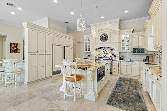 kitchen featuring sink, cream cabinetry, light stone counters, ornamental molding, and a kitchen island with sink