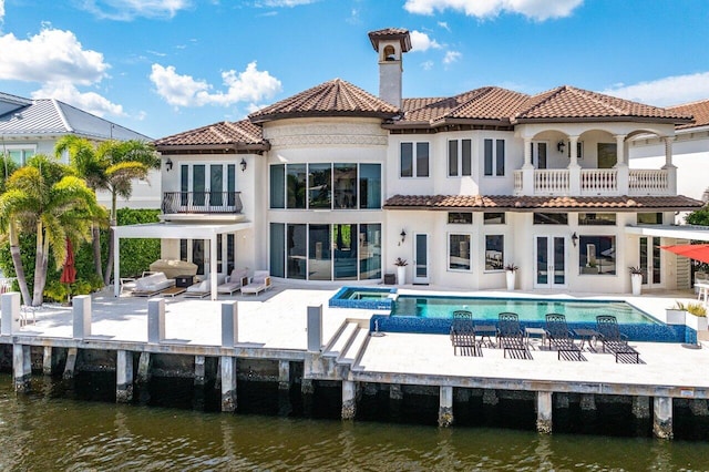 rear view of property featuring a patio, an outdoor living space, a water view, and a balcony