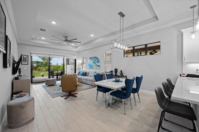 dining space featuring light hardwood / wood-style floors, a tray ceiling, crown molding, and ceiling fan