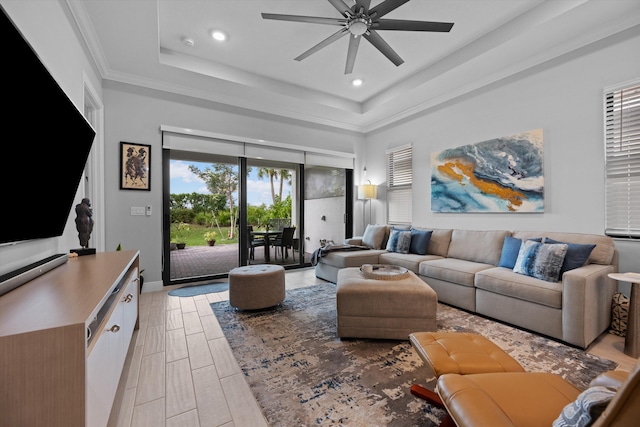 living room featuring ceiling fan, a tray ceiling, light wood-type flooring, and ornamental molding