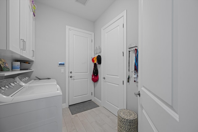 clothes washing area featuring cabinets, washing machine and dryer, and light wood-type flooring