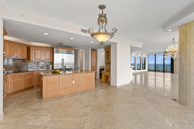 kitchen with stainless steel built in refrigerator, a notable chandelier, an island with sink, pendant lighting, and decorative backsplash