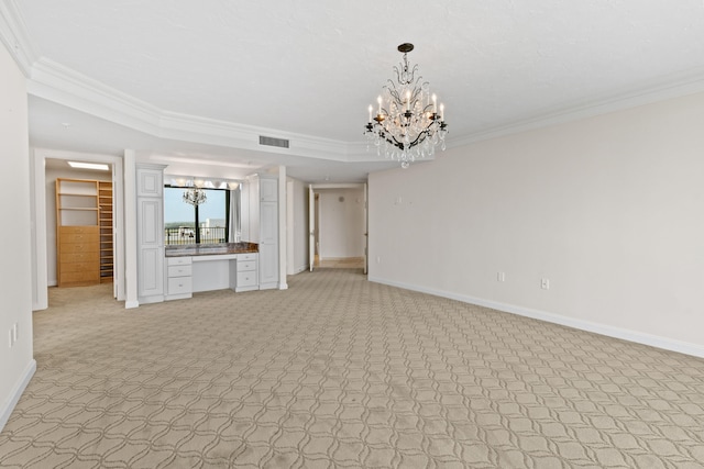 unfurnished living room featuring light colored carpet, built in desk, ornamental molding, and a chandelier