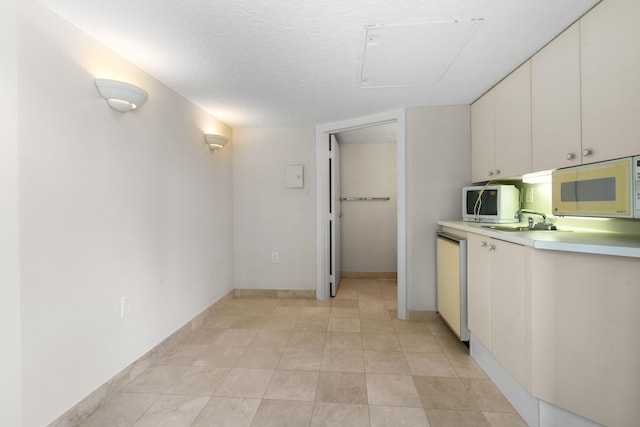 kitchen featuring white appliances, sink, a textured ceiling, light tile patterned flooring, and white cabinetry