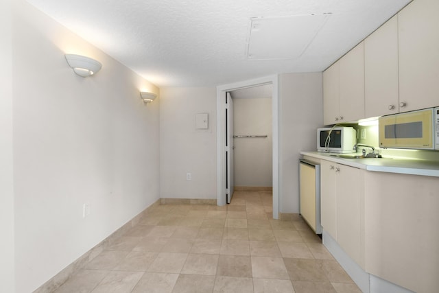 570 Ocean Dr Unit 1302, Juno Beach, FL 33408 - kitchen with white microwave, light countertops, dishwashing machine, white cabinetry, and a sink