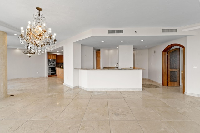 kitchen with an inviting chandelier, double oven, crown molding, dark stone counters, and pendant lighting