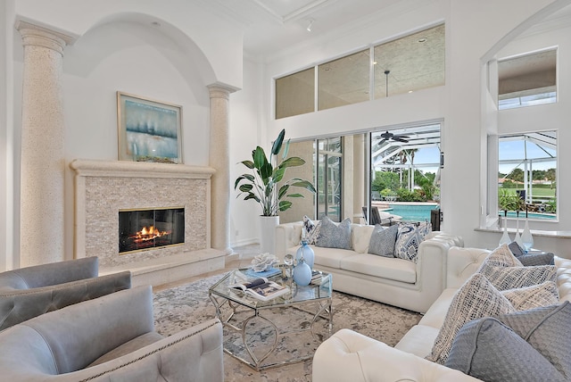 living room with a towering ceiling, ornamental molding, ornate columns, and ceiling fan