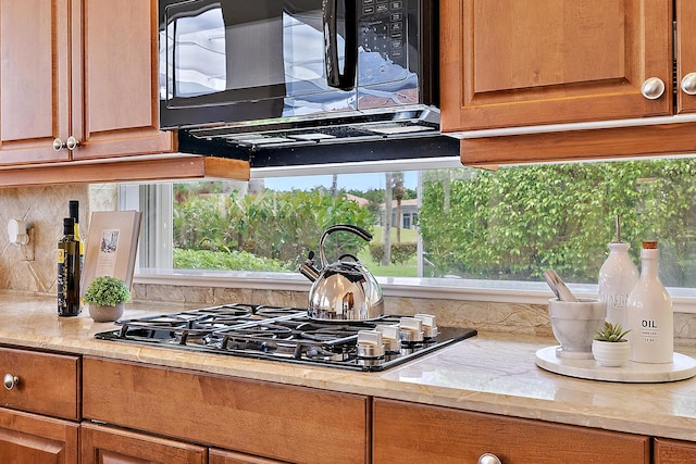 kitchen featuring stainless steel gas stovetop, light stone countertops, and backsplash