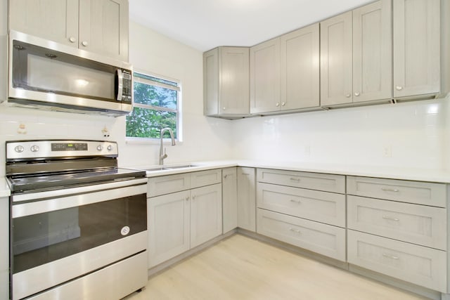 kitchen featuring sink, tasteful backsplash, light hardwood / wood-style flooring, gray cabinets, and appliances with stainless steel finishes