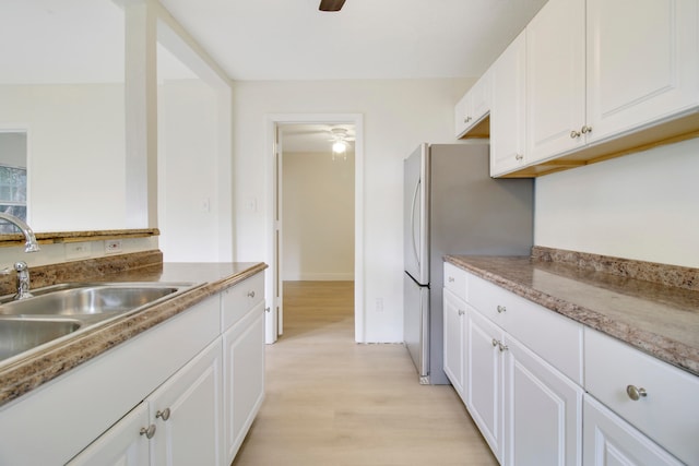 kitchen with light wood-type flooring, ceiling fan, stainless steel refrigerator, sink, and white cabinetry