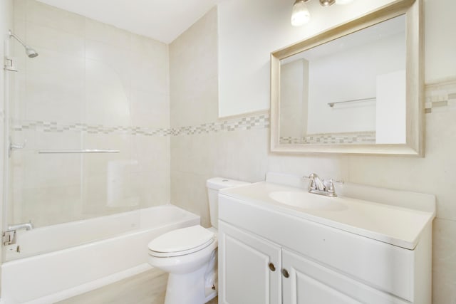 full bathroom with tiled shower / bath, vanity, tile walls, and toilet