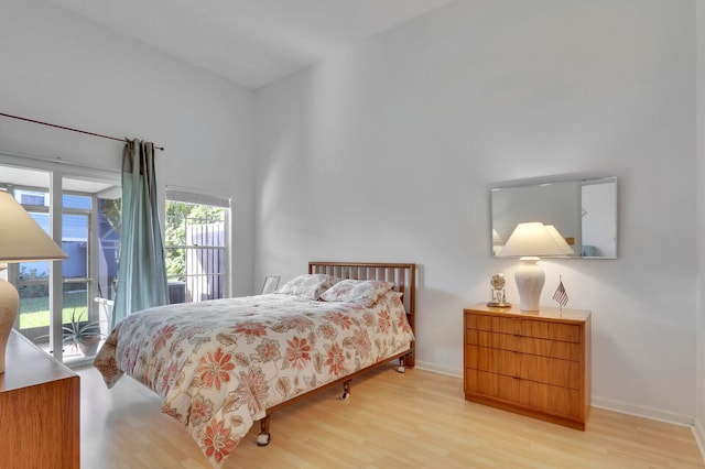 bedroom with a towering ceiling, light hardwood / wood-style flooring, and access to exterior