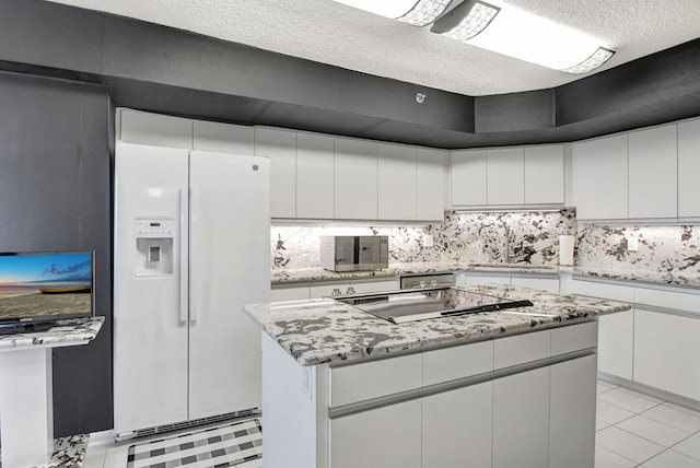 kitchen featuring sink, white refrigerator with ice dispenser, a kitchen island, white cabinets, and black stovetop