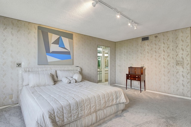 bedroom with ensuite bathroom, light colored carpet, rail lighting, and a textured ceiling