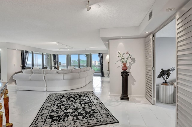 living room with a textured ceiling, light tile patterned floors, track lighting, and a raised ceiling