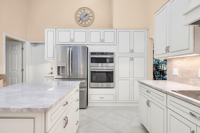 kitchen with stainless steel appliances, light stone countertops, light tile patterned floors, white cabinets, and a center island