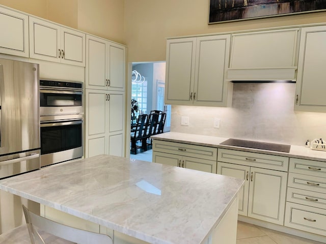 kitchen with light stone counters, tasteful backsplash, a kitchen breakfast bar, appliances with stainless steel finishes, and light tile patterned floors