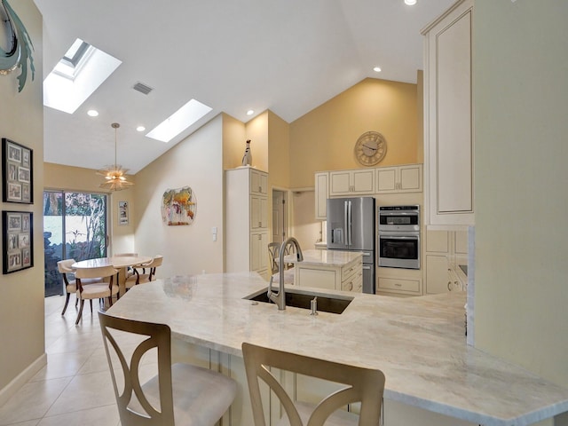 kitchen featuring pendant lighting, cream cabinetry, sink, stainless steel appliances, and light stone countertops