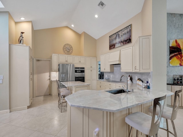 kitchen featuring light stone countertops, sink, kitchen peninsula, appliances with stainless steel finishes, and a kitchen breakfast bar