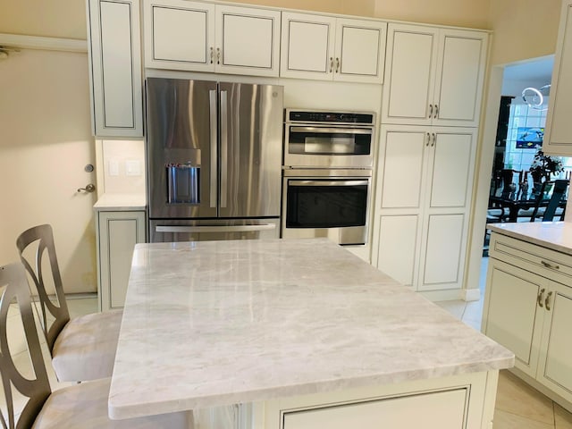 kitchen with light tile patterned floors, light stone counters, a kitchen breakfast bar, and stainless steel appliances