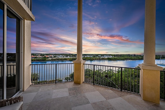 balcony at dusk featuring a water view