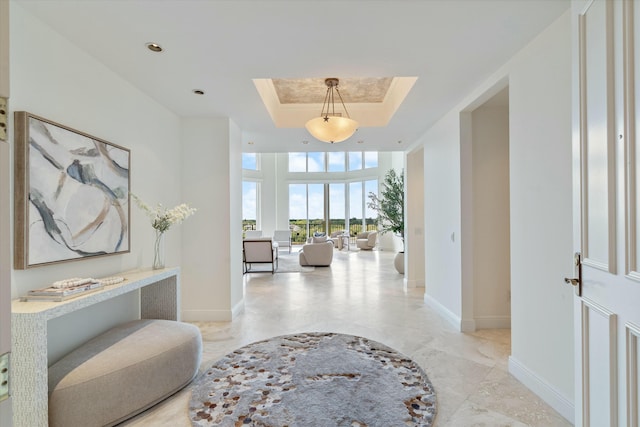 hall featuring a skylight, baseboards, a towering ceiling, marble finish floor, and a tray ceiling